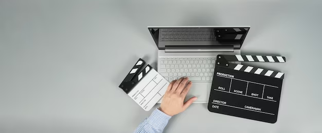 Person using a laptop with a black clapperboard/movie slate on a gray background